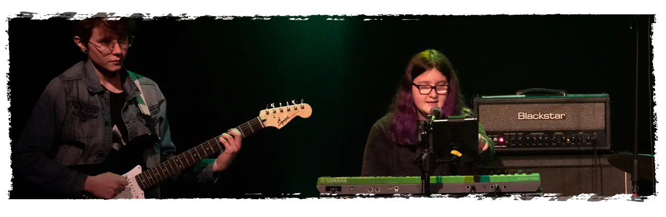 musique-collaboration-jeunes Deux adolescents jouent de la guitare électrique et du clavier en groupe, illustrant les bienfaits éducatifs de la musique.